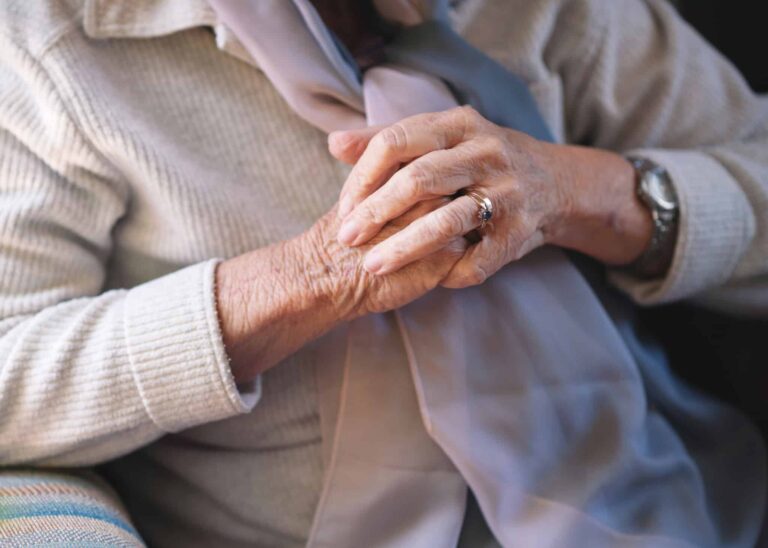 Closeup, hands together and elderly woman with retirement, relax in a living room and peaceful on a weekend break